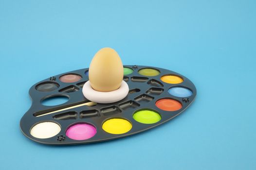 Easter egg decoration concept with blank blackboard and set of watercolor paints in pallet. Studio still life on blue background