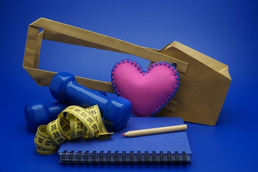 Going shopping for sports diet concept still life with dumbbells, measuring tape and notebook on blue background