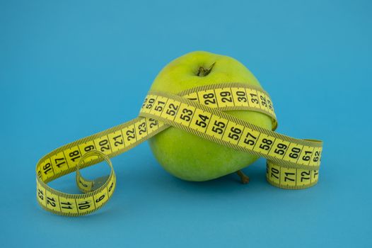 Weight loss and healthy diet concept with measuring tape and green apple on blue background