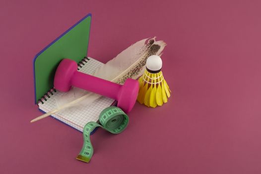 Sport weight loss and fitness concept with a shuttlecock, dumbbell weight and tape measure alongside an open notebook with quill pen on a bright pink background