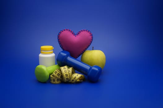 Still life with small dumbbells, measuring tape and fruits, as a concept of healthy nutrition and sports diet in close-up on blue background