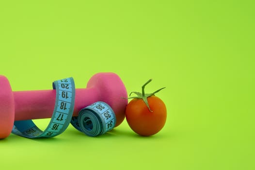 Still life with dumbbell, measuring tape and cherry tomato, as a concept of healthy nutrition and sports diet in close-up on green background and free copy space