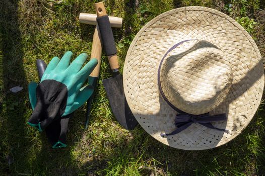 Straw sunhat with gloves and gardening tools lying on a green lawn in a spring garden in the sunshine conceptual of the seasons viewed top down