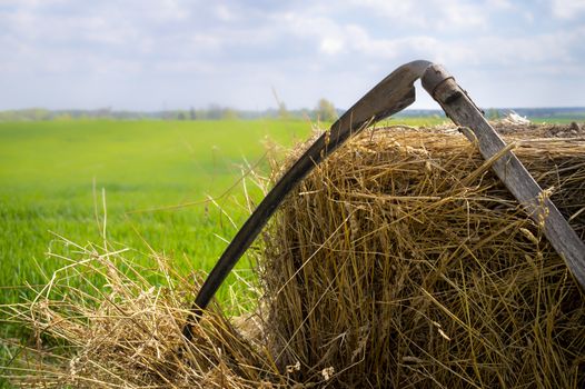 Scythe resting up against freshly harvested hay in a lush green farm field in spring in an agricultural landscape