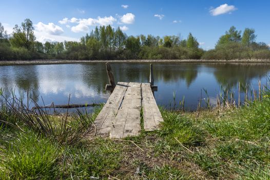 Old rustic wooden jetty on a tranquil lake with wild grasses on the bank and reflections on the water