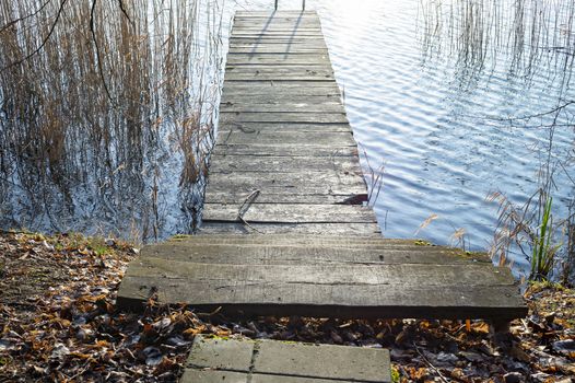 Old rustic wooden steps leading to a jetty over the calm water of a lake with reeds looking down from the top