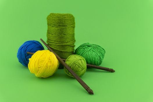 Green, blue and yellow knitting yarn or wool on colorful green background with knitting needles