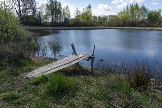 Old rustic wooden jetty on a tranquil lake with wild grasses on the bank and reflections on the water