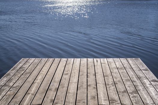 Wooden textured boards of a jetty and reflection of the sun on the water in a low angle view