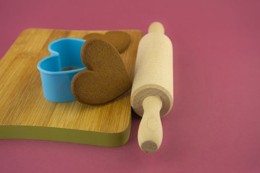 Preparing heart-shaped cookies to a loved one concept with red envelope on pink background with copy space