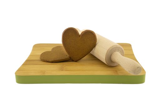 Heart-shaped cookies gift preparation concept with brown biscuits and rolling pin on wooden cutting board isolated on white background