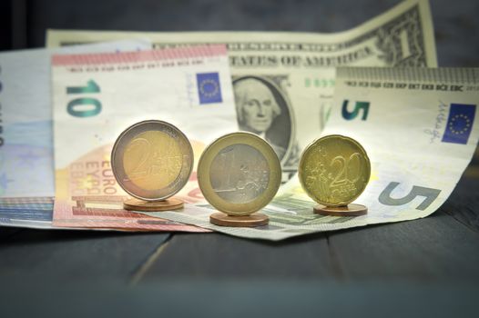 Close-up of Euro and USD cash money with various coins of Euros and cents over banknotes on black wooden table. Strong and stable currency concept with dollar bill and variety of Euro bills