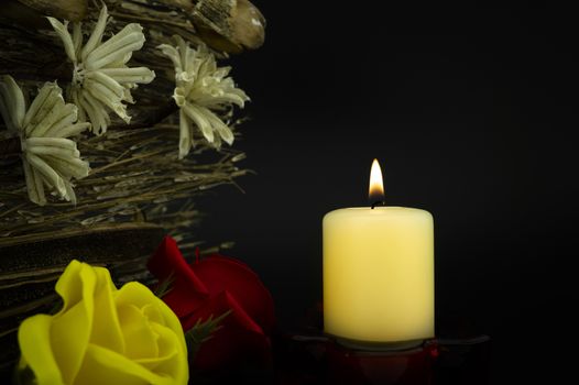 A close up of an orange candle and flame among flowers on a dark background