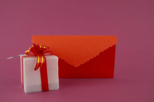 Romantic still life with decorative gift and red envelope on pink background with copy space