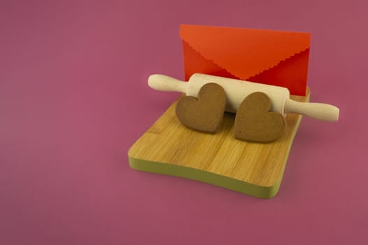 Message with love concept with two heart shaped cookies and red envelope on pink background with copy space