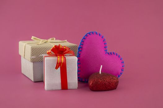 Romantic still life with hand sewn textile pink heart, candle, decorative gifts and red envelope on pink background with copy space