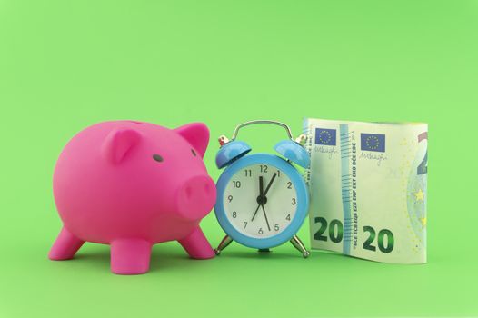Time management and financial success concept with a 20 Euro bill alongside an alarm clock with piggy bank in the background over green
