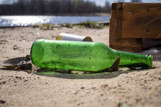 Old discarded empty green bottle and tin can lying in the shoreline of a lake conceptual of household pollution