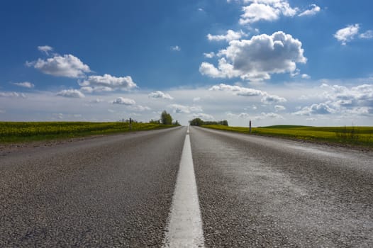 Low angle view of a tarred road receding into the distance in open countryside under a cloudy blue sky with focus to the center white line