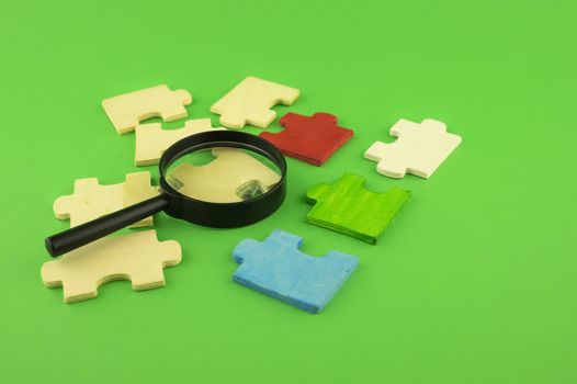Selection of jigsaw puzzle pieces with magnifying glass on a green background with copy space conceptual of a search, teamwork and problem solving