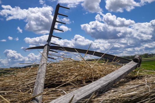 Rake and scythe on dried straw against a sunny blue sky with white clouds