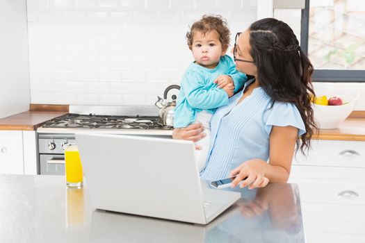 Smiling brunette holding her baby in the kitchen