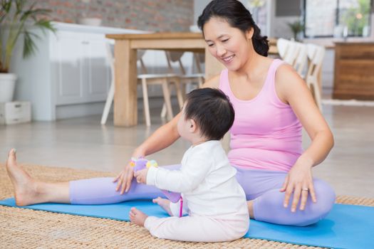 Happy mother exercising on mat while looking at baby daughter at home