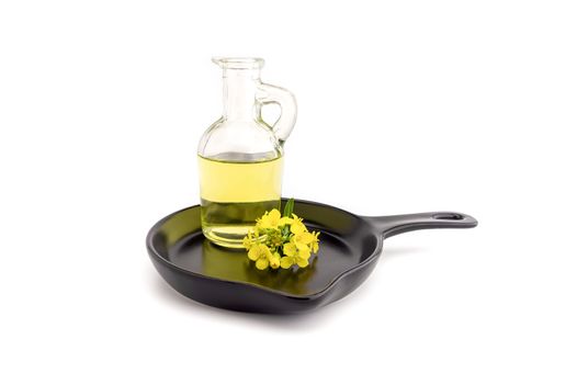 Small sprig of vivid yellow mustard or rapeseed flowers with decanter of oil on a cast iron skillet over a white background with copy space