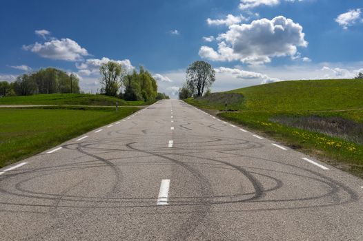 Rubber marks from wheelies on a road surface between lush green fields on a sunny day