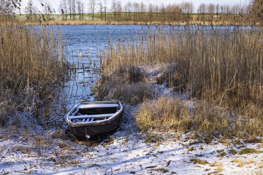 Old fishing boat among the reeds on the bank of a frozen river in winter, waiting on its time. Waiting for season concept