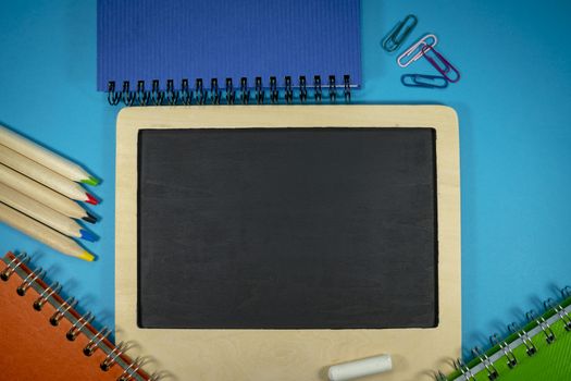 September still life with chalks and chalk board, spiral ring bound notebooks, pencils and scattered paper clips. Flat lay, view from above