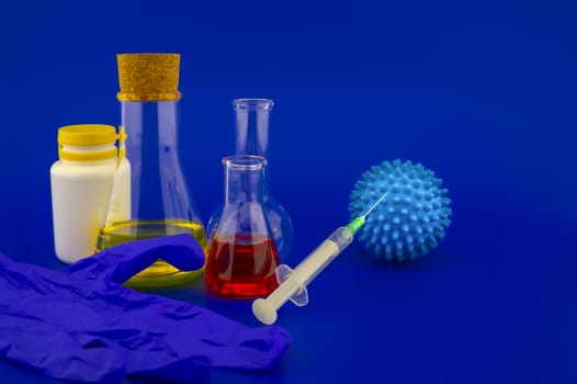 Concept of research for a Covid-19 vaccine with a conical lab flasks with yellow and red solutions alongside a hypodermic syringe and blue virus molecules over a blue background with copy space