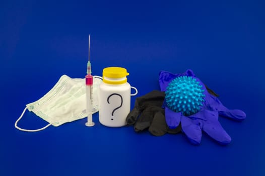 Various medical supplies including a hypodermic syringe, pharmaceutical bottle and face mask with a corona virus model and blue copy space