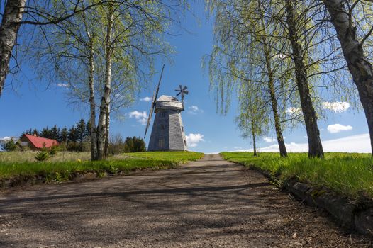 Picturesque empty country road leading to an old historic windmill in rural area. Countryside landscape shot from low angle against blue sky in spring