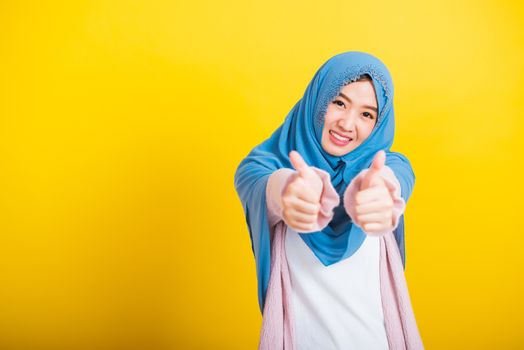 Asian Muslim Arab, Portrait of happy beautiful young woman Islam religious wear veil hijab funny smile she made finger thumbs up, Ok sign to agree, studio shot isolated on yellow background