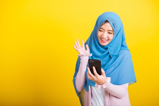 Asian Muslim Arab, Portrait of happy beautiful young woman Islam religious wear veil hijab funny smile she selfie or video call mobile smart phone raise hand say hello isolated on yellow background