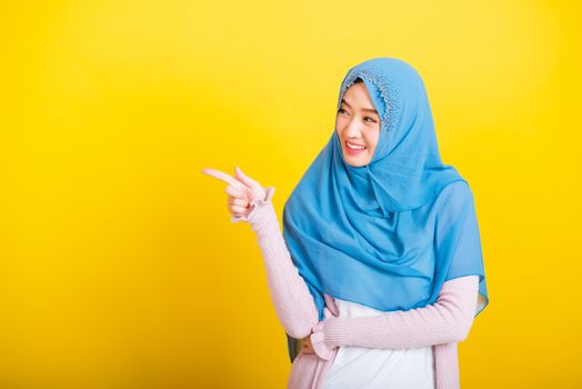 Asian Muslim Arab, Portrait of happy beautiful young woman Islam religious wear veil hijab funny smile she positive expression pointing finger side sideways to space isolated yellow background