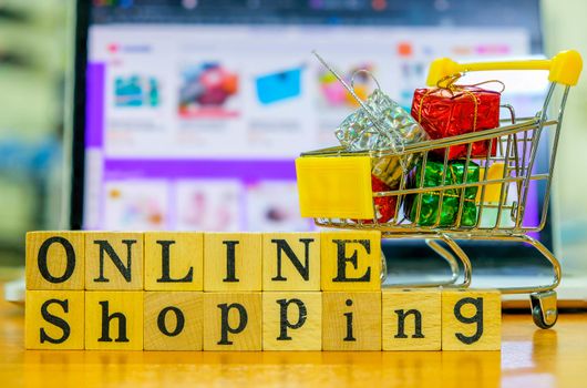 Wooden Alphabet "online shopping" and shopping cart in front of the Blured Shopping Online Website