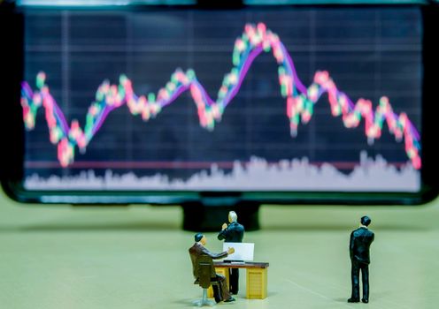 Miniature figure business people or Stock Trader looking at Blur Stock board for Graph Analysis