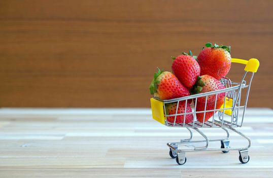 Close up strawberry on shopping cart with white and brown wooden background,text advertising, diet food healthy food
