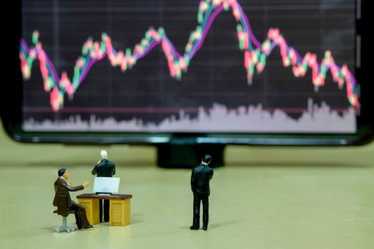 Miniature figure business people or Stock Trader looking at Blur Stock board for Graph Analysis