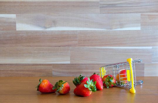 Close up strawberry on shopping cart with white and brown wooden background text advertising, diet food healthy food