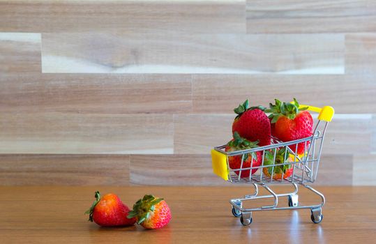 Close up strawberry on shopping cart with white and brown wooden background text advertising, diet food healthy food