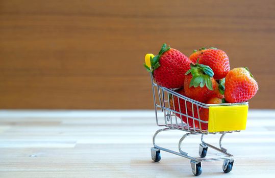 Close up strawberry on shopping cart with white and brown wooden background,text advertising, diet food healthy food