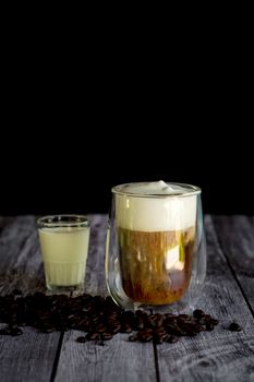 Coffee time and refreshment concept. Transparent glass of coffee with milk froth and roasted coffee bean on wooden background.