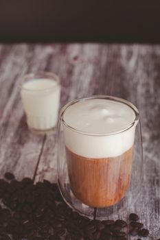 Coffee time and refreshment concept. Transparent glass of coffee with milk froth and roasted coffee bean on wooden background.