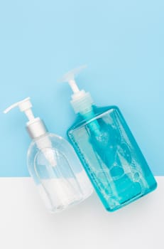 White and blue bottles of sanitizer or liquid soap for hand hygiene to protect from corona virus over two tone background,flat lay