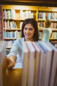 Smiling brunette picking out a book of bookshelves in library