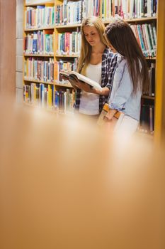 Pretty young students working together with book in library