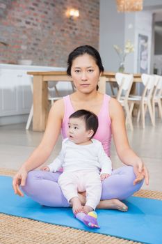 Serious woman sitting on mat with baby daughter at home